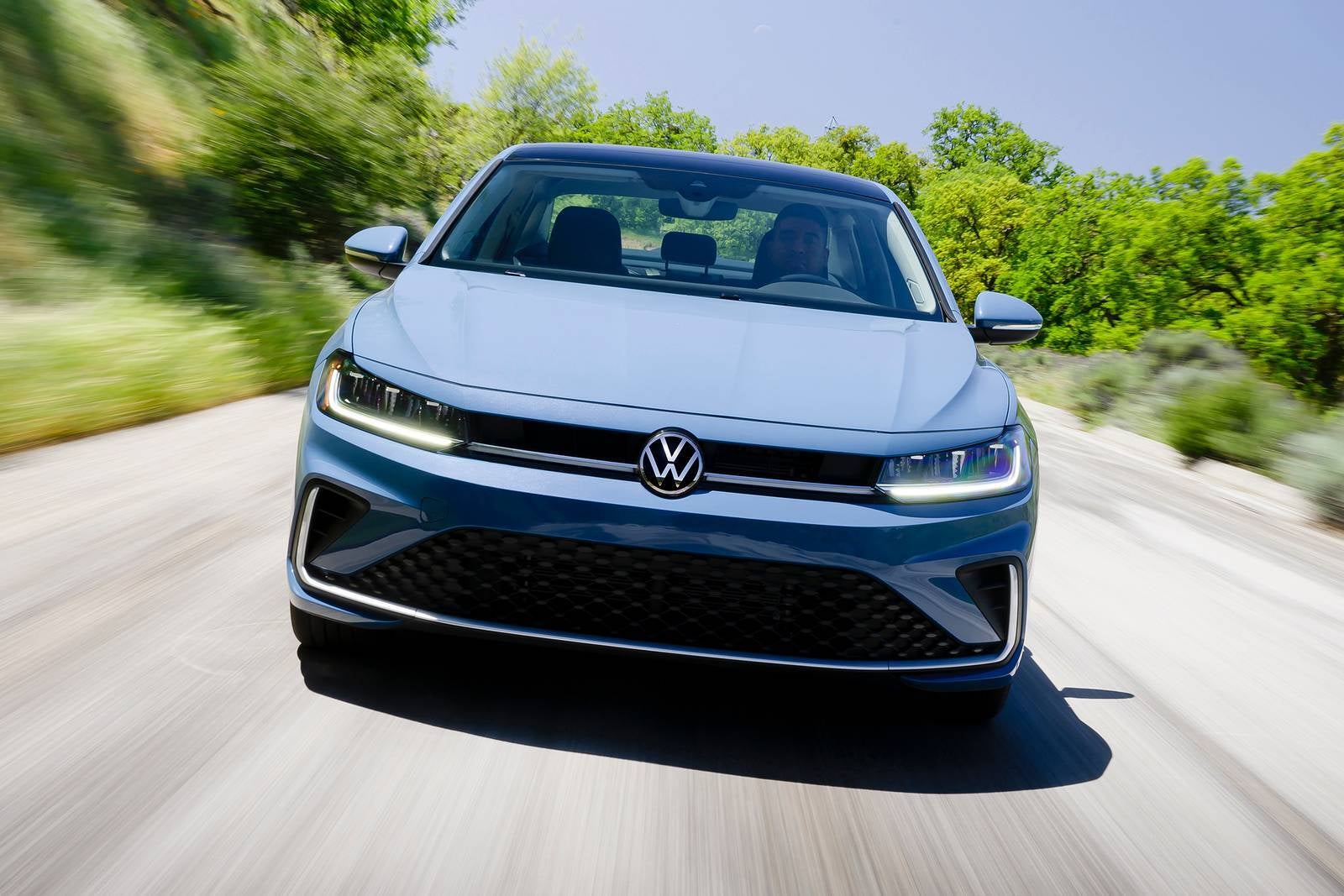 A blue jetta driving on the road.