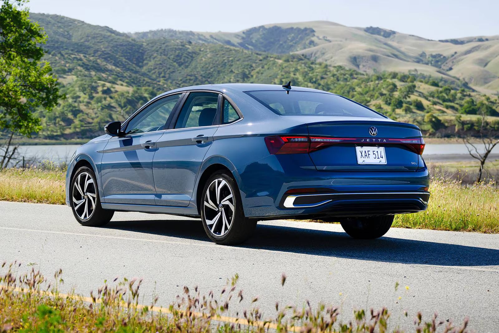 A blue jetta sitting in the road.