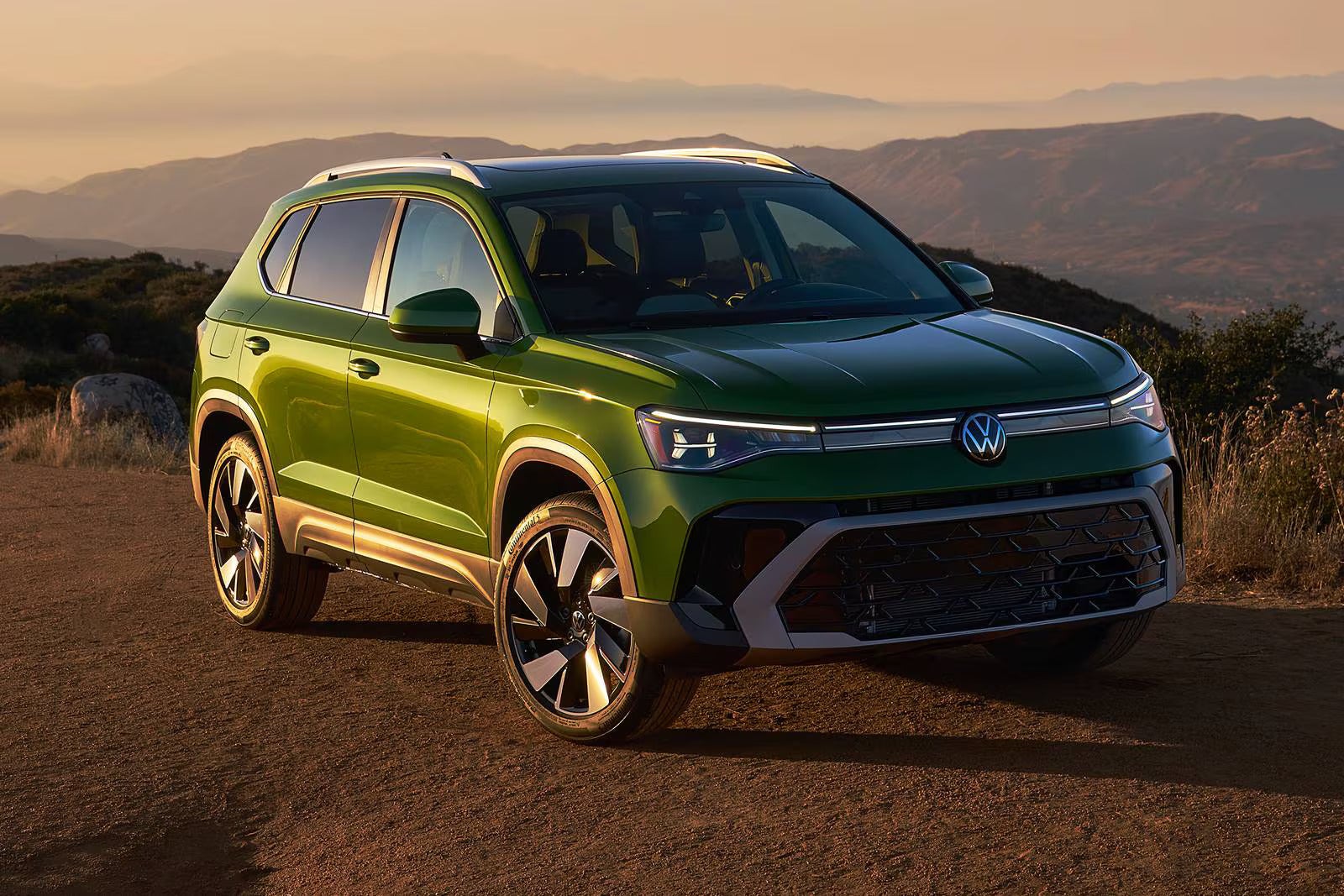 A green suv sitting parked on a dirt road.