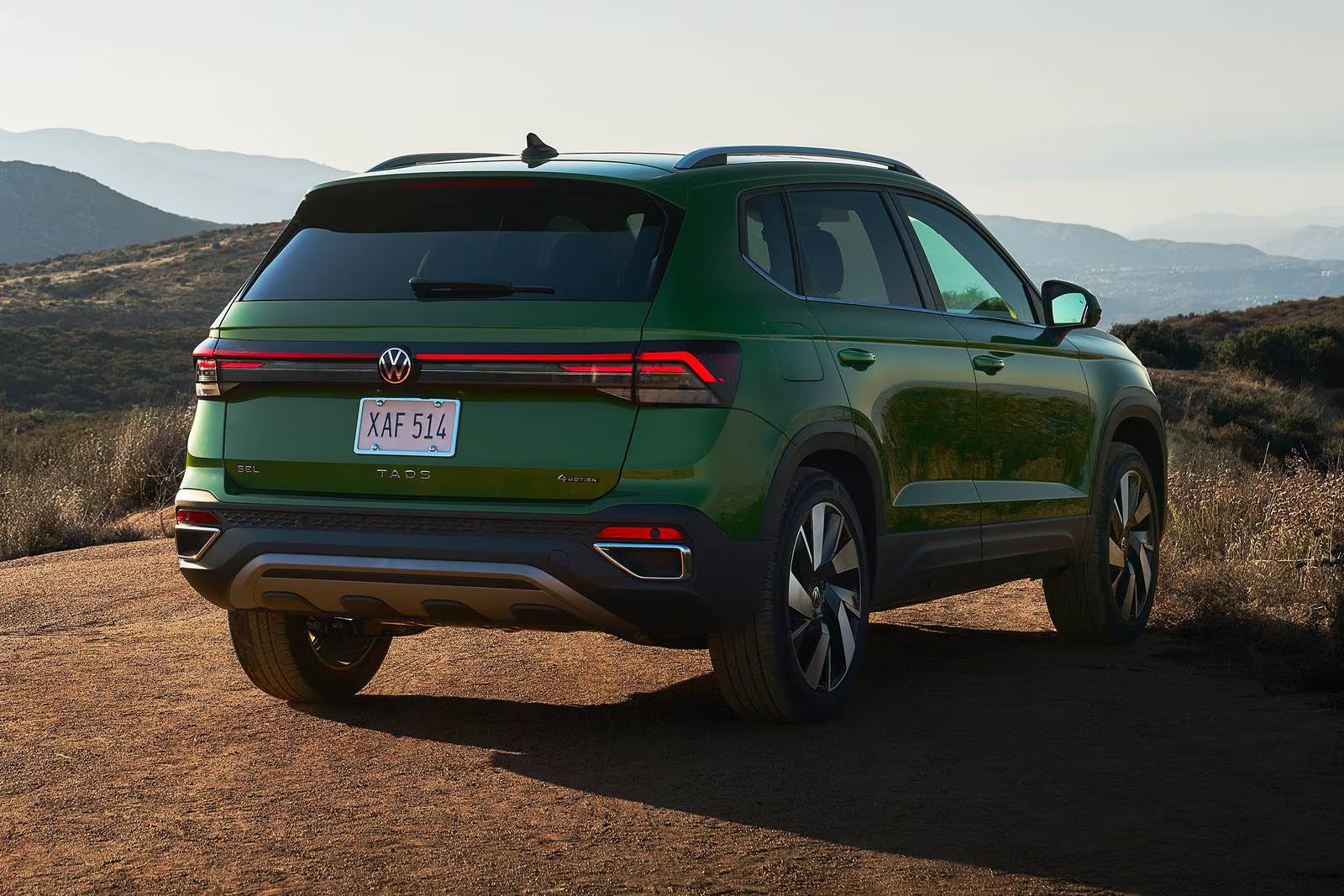 A green suv sitting parked on a dirt road with the rearend facing.